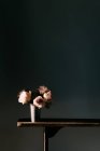 Roses roses fraîches en fleurs dans un vase vintage placé sur une table en bois au mur noir dans un appartement moderne — Photo de stock