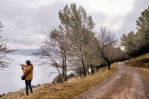 Full body male traveler in warm outwear standing on remote shore of lake in autumn season and admiring amazing landscape with cloudy mountains — Stock Photo