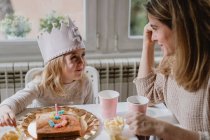Positive mother in casual clothes sitting at wooden table and talking with kids celebrating birthday at home — Stock Photo