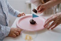 Безликая женщина делится сладким шоколадным десертом с флагом на розовой тарелке с детьми дома — стоковое фото