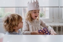 Garota encantadora excitada na coroa artesanal desembrulhando caixa de presente ao ter celebração de aniversário em casa — Fotografia de Stock
