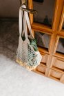 White string bag with fresh loquat fruit and leaves hanging on door — Stock Photo