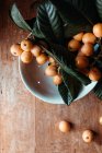 White ceramic bowl with tasty loquat fruit and leaves — Stock Photo