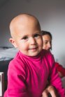 Mignon petit garçon en chemise rose décontractée debout sur le sol dans la salle de jeux lumière et en regardant la caméra tout en passant du temps à la maison — Photo de stock