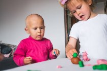 Милі веселі маленькі діти в повсякденному одязі граються з пластиліном, проводячи час разом вдома — стокове фото