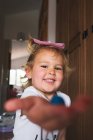 Ragazzina sorridente in camicia bianca casual che tiene in mano il giocattolo plasittico fatto a mano e raggiunge la fotocamera mentre gioca a casa — Foto stock