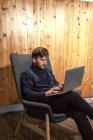 Empresario masculino sentado en la mesa de madera en un espacio de trabajo creativo y trabajando en un proyecto remoto mientras usa netbook - foto de stock