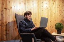 Imprenditore maschio seduto al tavolo di legno in uno spazio di lavoro creativo e che lavora su un progetto remoto durante l'utilizzo di netbook — Foto stock