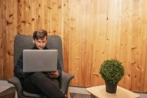 Male entrepreneur sitting at wooden table in creative workspace and working on remote project while using netbook — Stock Photo