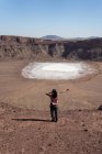 Back view female traveler pointing at sodium phosphate crystal surface inside crater during trip in desert valley with rocky terrain — Stock Photo