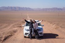 Vista a distanza di allegro giovane uomo e donna in abbigliamento casual godendo di avventura durante il viaggio sul deserto ai piedi delle montagne — Foto stock