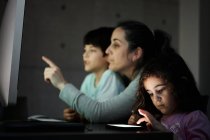 Glückliche junge Mutter mit kleinem Sohn und Tochter, die zu Hause am Tisch mit dem Computer sitzen — Stockfoto
