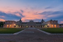 Facade of illuminated medieval palace with driveway and green lawns under sunset sky — Stock Photo