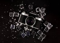 Top view of vintage photo camera surrounded by ice cubes showing concept of well preserved gadget on black background — Stock Photo