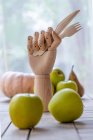 Деревянная рука с ножом и вилкой помещена на стол со свежими фруктами и овощами для питательной диеты — стоковое фото