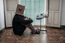 Uomo con scatola di cartone e calzini a righe seduto sul pavimento con macchina da scrivere retrò — Foto stock