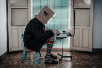 Mann mit Pappschachtel und gestreiften Socken sitzt auf Stuhl und tippt auf Retro-Schreibmaschine — Stockfoto
