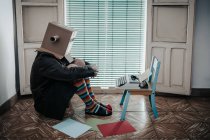 Homme portant boîte en carton et chaussettes rayées assis sur le sol par chaise avec machine à écrire rétro — Photo de stock