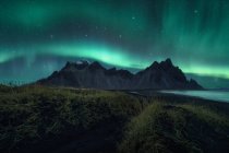 Increíble paisaje del norte con aurora boreal brillante en el cielo estrellado sobre las montañas rocosas del promontorio de Stokksnes en Islandia - foto de stock