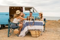 Smiling friends clinking bottles celebrating vacation near car in bright day — Stock Photo