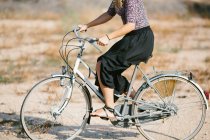 Crop female in summer outfit walking with bike in park on sunny day and looking away — Stock Photo