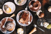Высокий угол Tiramisu украшен какао порошок помещен на стол с кексом и шоколадный торт посыпанный сахарной пудрой — стоковое фото