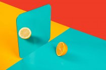 Fundo vibrante com reflexo de espelho de metade de laranja fresca como limão na superfície azul em composição com áreas vermelhas e amarelas vazias como conceito de percepção no espaço tridimensional e distorção da imaginação — Fotografia de Stock