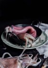Uncooked meat of squids placed in metal bowl on table in kitchen on black background — Stock Photo
