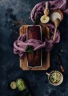 Draufsicht auf leckeren Schokoladenkuchen mit Blütenblättern und Basilikum garniert und auf den Tisch mit grünen Zucchini und saurer Sahne in Schüssel gelegt — Stockfoto