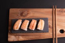 Blick von oben auf köstliches Sushi mit Reis und Garnelen, serviert auf Holzbrett mit Essstäbchen im Restaurant — Stockfoto