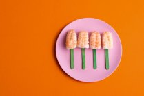 Верхний вид аппетитного набора эби нигирских суши с креветками, подаваемых в форме эскимо и помещенных на тарелку на оранжевом фоне в студии — стоковое фото