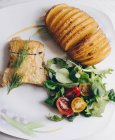 Top view of delicious baked Hasselback potatoes and fresh vegetable salad served with roasted chicken fillet garnished with sprig of dill — Stock Photo