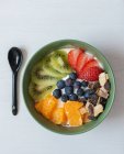 De cima de delicioso café da manhã saudável com kiwi fatiado e laranjas colocadas em tigela com mirtilos e morangos — Fotografia de Stock