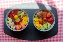 Draufsicht auf Schüsseln mit gehacktem frischem Gemüse und Fleisch von Lachs und Huhn, die in der Küche zum Mittagessen auf den Tisch gestellt werden — Stockfoto