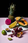 Still life with tropical fruits: sliced papaya, pineapple, pitaya and grapes on marble cutting board — Stock Photo