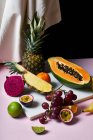Still life with tropical fruits: sliced papaya, pineapple, pitaya and grapes on marble cutting board — Stock Photo