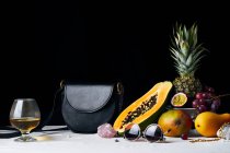 Natura morta con frutta tropicale, gemme, borsa in pelle nera e vari oggetti — Foto stock