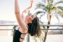 Грациозная танцовщица в момент исполнения элемента с вытянутыми руками, смотрящая на летнюю террасу на фоне пальм — стоковое фото