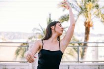 Anmutige Tänzerin im Moment des darstellenden Elements mit ausgestreckten Armen und geschlossenen Augen auf der Sommerterrasse vor Palmen — Stockfoto