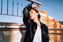 Serene female in trendy leather jacket standing on summer terrace with closed eyes and enjoying sunny weather — Stock Photo