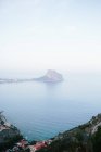 Vue aérienne du littoral rocheux avec îlot au milieu de la mer près de la baie de la mer avec eau bleue calme contre ciel nuageux et horizon dans la brume légère pendant la journée — Photo de stock