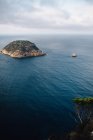 Aerial view of rocky coastline with islet in the middle of the sea close to sea bay with calm blue water against cloudy sky and horizon in light haze at daytime — Stock Photo