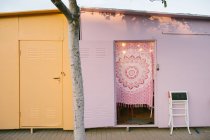 Shabby ha alterato le case metalliche gialle e rosa situate sul marciapiede dietro l'albero nella zona urbana durante la giornata estiva soleggiata con cielo blu chiaro — Foto stock