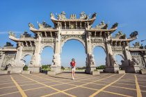 Знизу струнка жінка - мандрівник фотографує фотоапарат, стоячи на тротуарі біля фасаду китайського храму з арками, прикрашеними скульптурами. — стокове фото