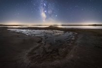 Empty dry soil road among calm water under colorful nigh sky with milky way on background — Stock Photo
