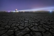 Silhueta de homem irreconhecível de pé com tocha na mão sobre a superfície seca rachada do solo estendendo-se para um céu estrelado noite colorida no horizonte — Fotografia de Stock