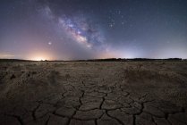 Суха тріщина поверхні землі і барвисте нічне зоряне небо на горизонті — стокове фото