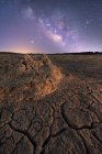 Seco superficie agrietada del suelo y colorido cielo estrellado noche en el horizonte - foto de stock