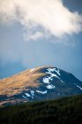 Вид на гору, вкритий снігом серед зелених пагорбів з лісом проти хмарного неба навесні в Шотландському нагір 