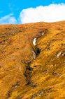 Vue pittoresque de la pente de montagne couverte de neige parmi les collines verdoyantes avec forêt contre ciel nuageux au printemps dans les Highlands écossais — Photo de stock